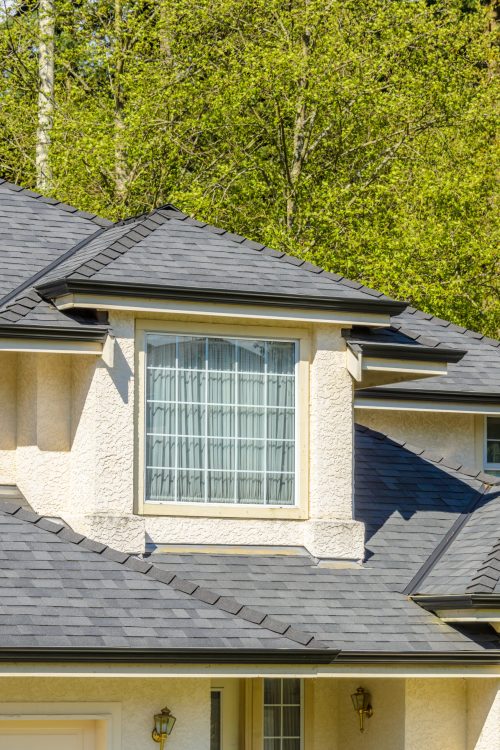 Top of grey stucco luxury house with shingle roof, red and yellow trees and nice windows in Summer in Vancouver, Canada, North America. Day time on June 2024. The roof of the house with nice window.